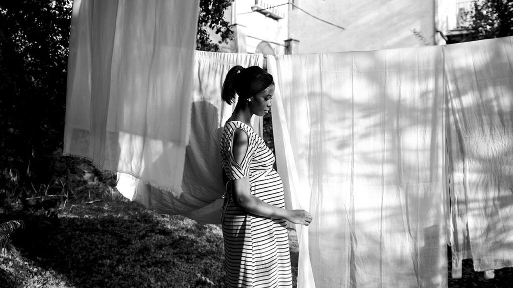 Black and white image of a pregnant person hanging out laundry outside