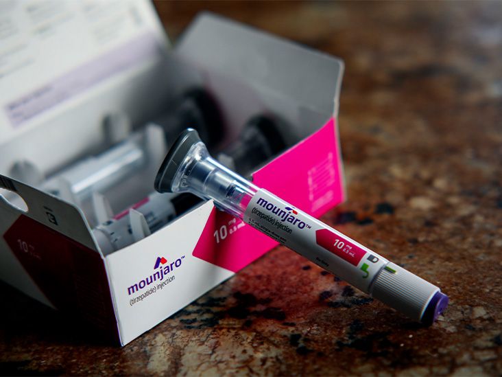 A Mounjaro injector pen rests on top of a pink and white Mounjaro box.