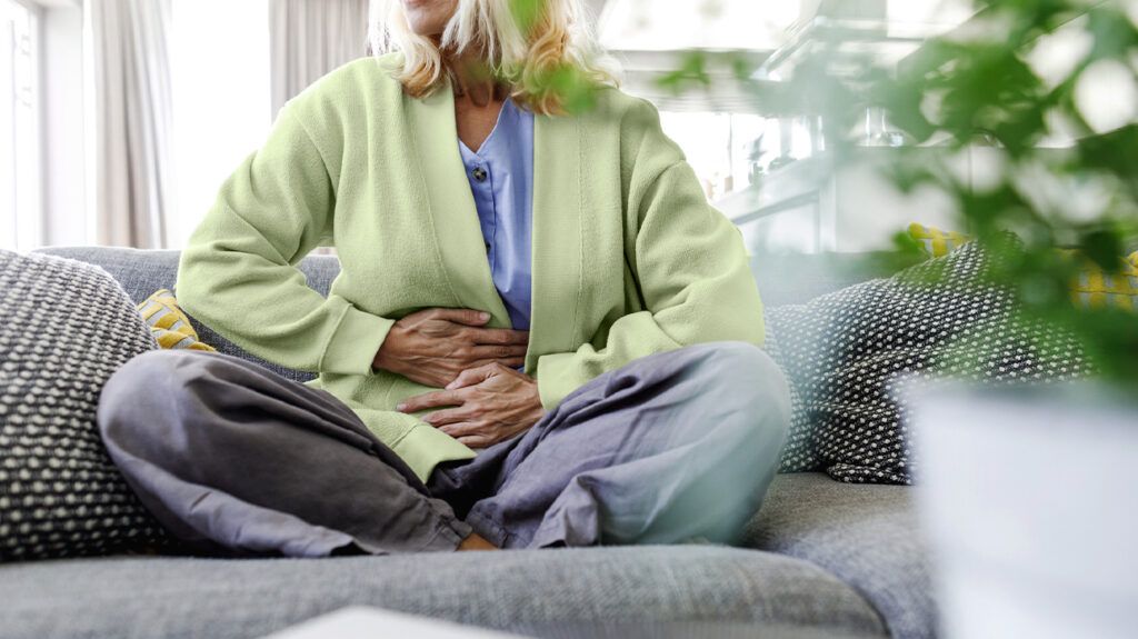 Woman with stomach ache, sitting on a sofa.