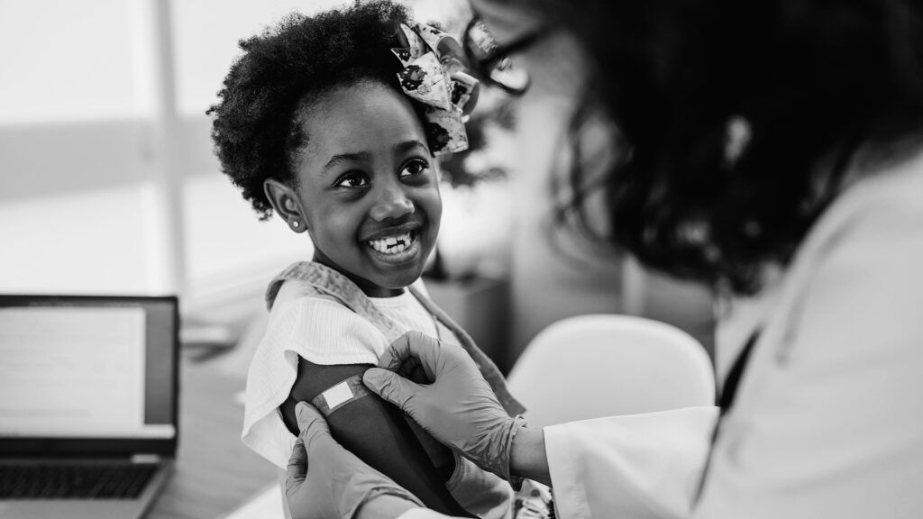 A Black child receives a flu vaccine shot on their arm at a doctor's office