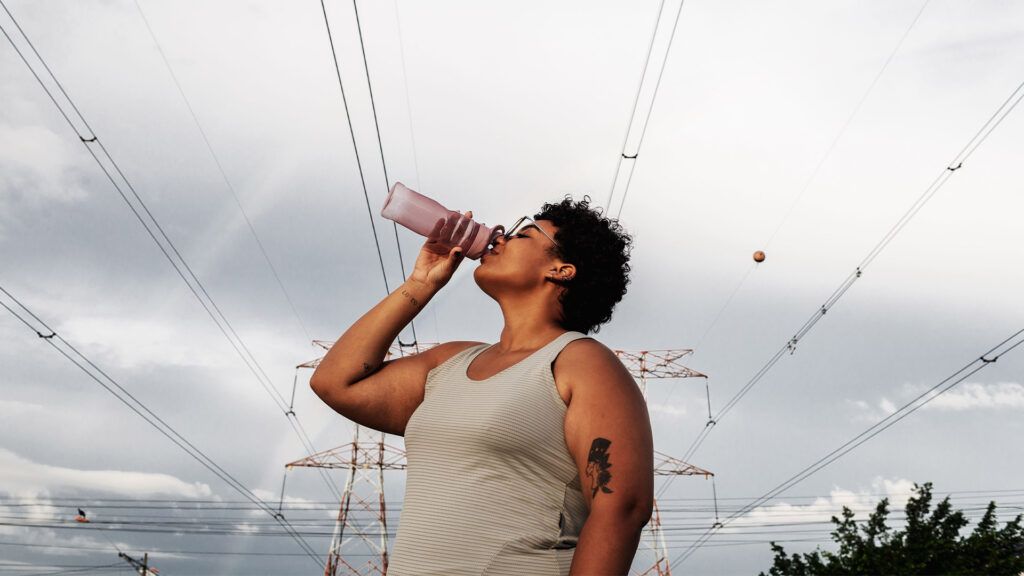 A woman drinks from a water bottle while standing under some power lines