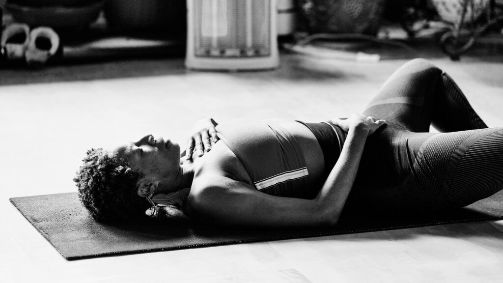 A woman lying down on a blue yoga mat practicing deep breathing for migraine.