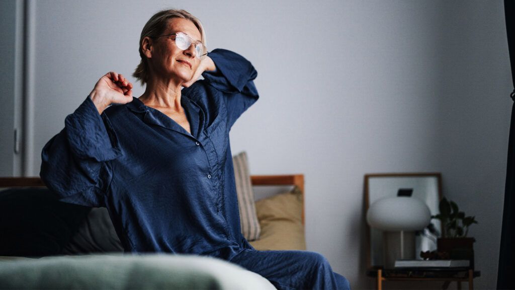 older woman in blue pyjamas stretching on a bed