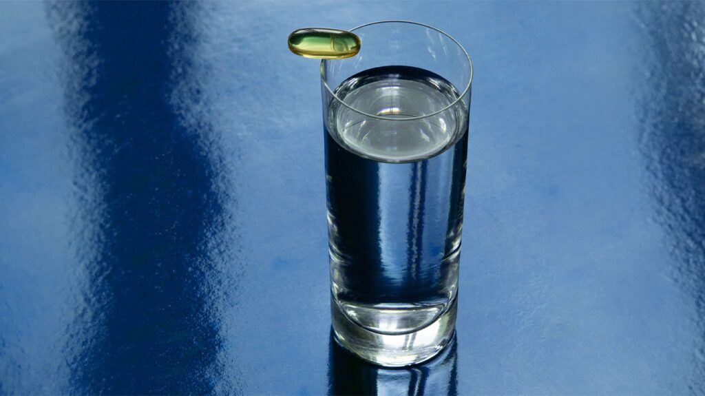 A fish oil supplement resting atop a glass of water