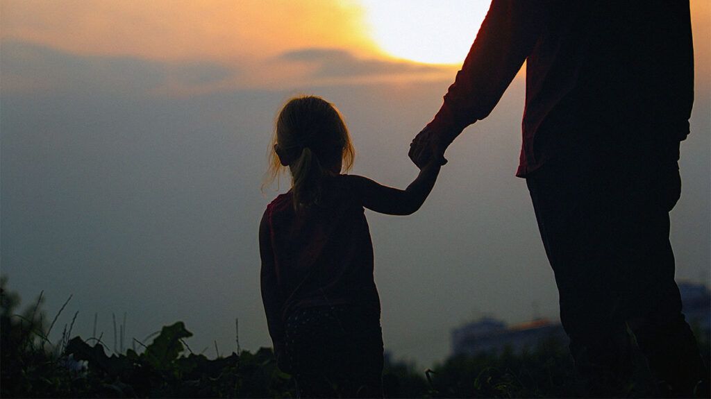 Silhouette of an adult and child holding hands in a sunset