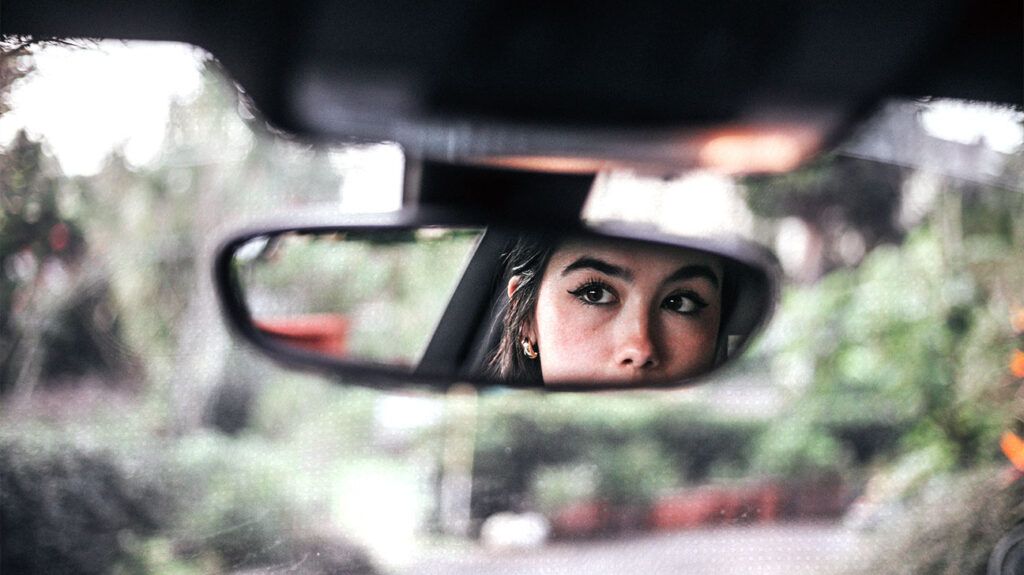 A woman with macular hole reflected in a rearview mirror in a car.-1