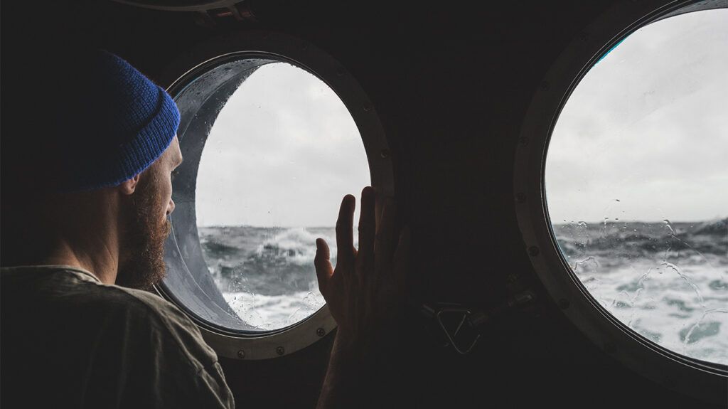 Person looking at the sea through the porthole of a ship