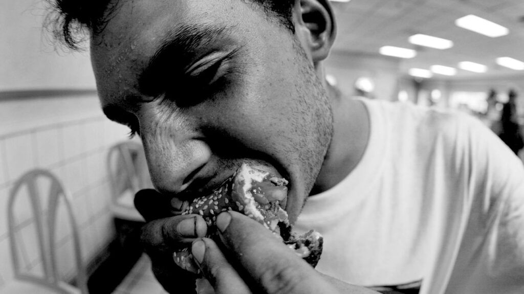 black and white photo of young white man biting into a burger