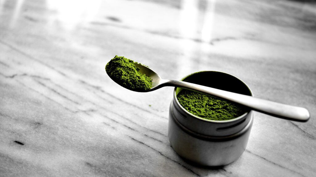 cylindrical pot of matcha powder and silver teaspoon