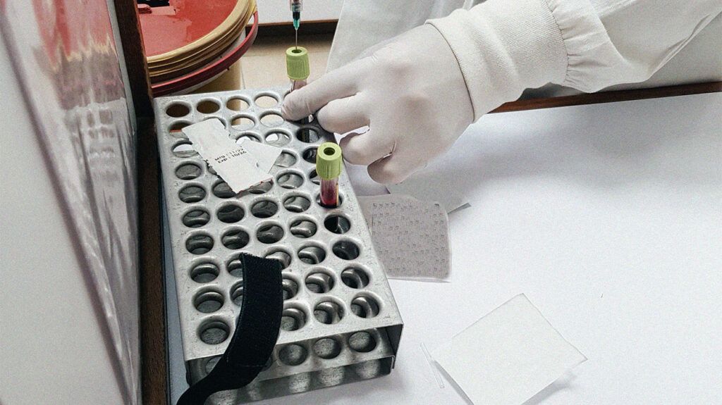 Person's gloved hands transferring sample vials to a holder in a lab