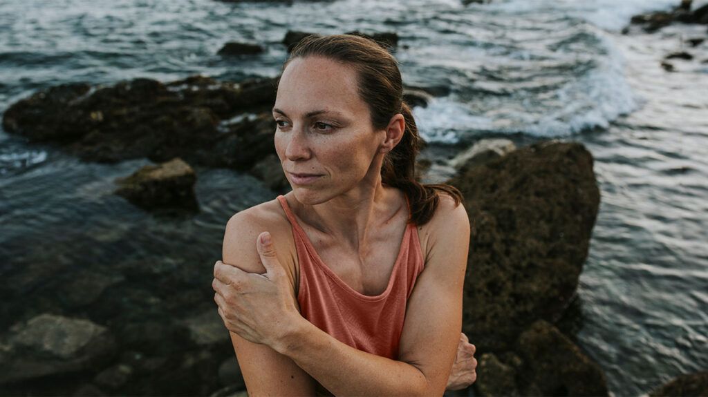 A pensive woman sits along a rocky shore
