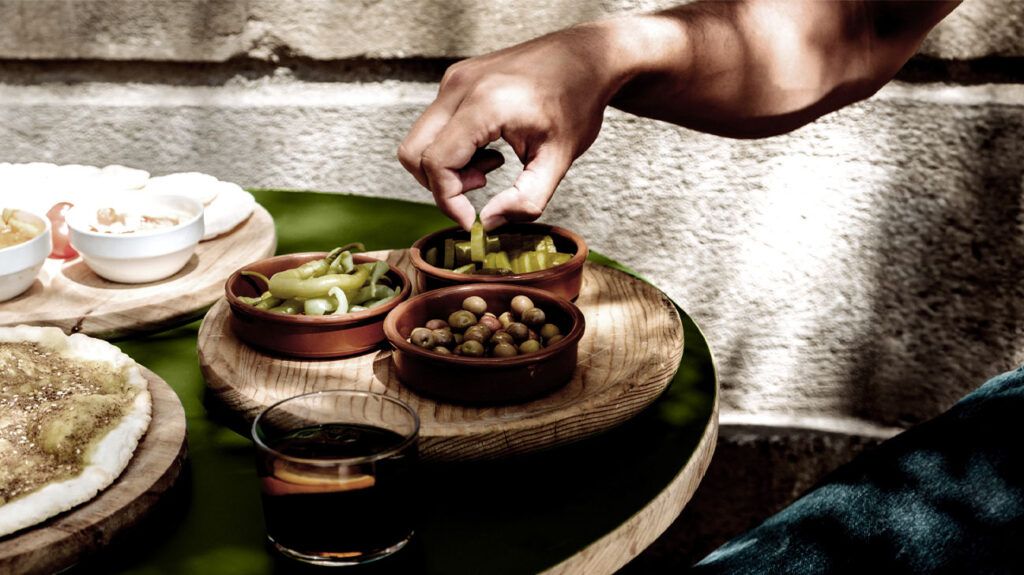 A person picks olive tapas from bowls on a table