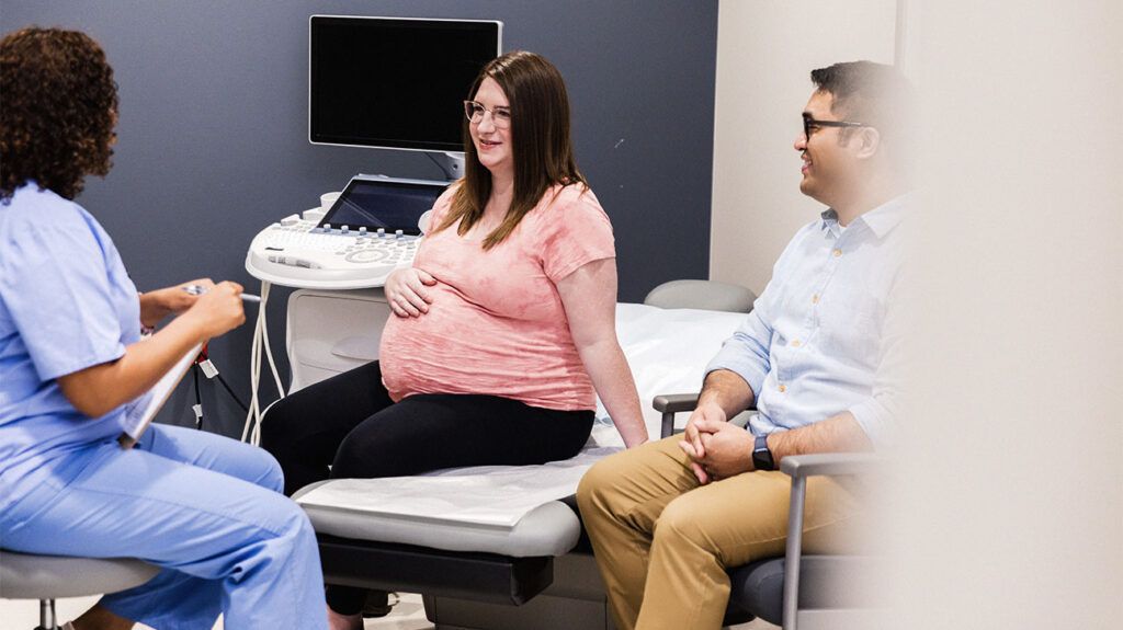 A pregnant person sitting in a doctor's office and speaking with a nurse about kidney disease.-2