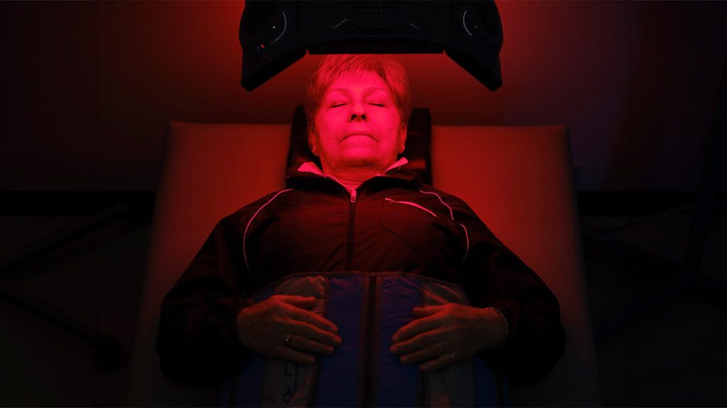 A person lying down in a medical setting, receiving red light treatment