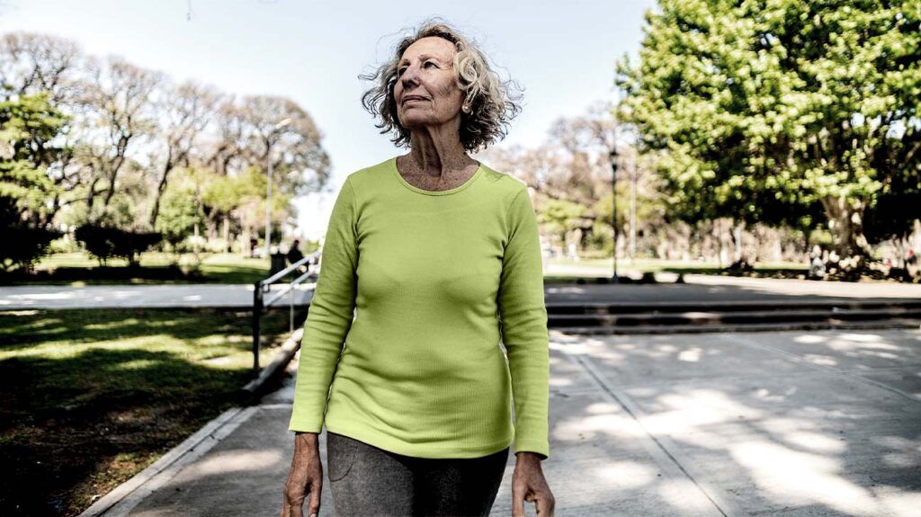 older white woman in green shirt walking in a park