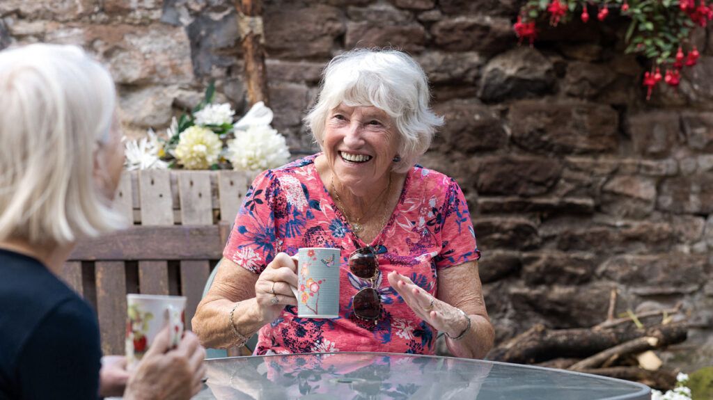 Two older people talking and having tea outside 1