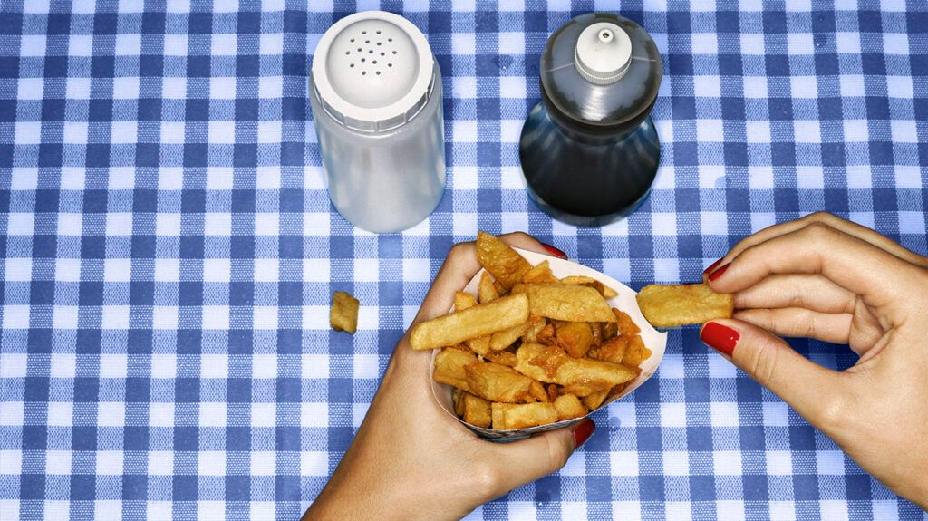 a person holding a bag of french fries next to table salt and seasoning on a dining table
