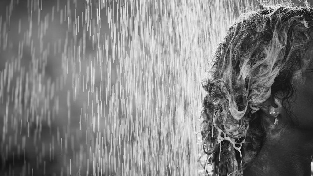 A woman with shampoo in her hair under a rainfall shower.