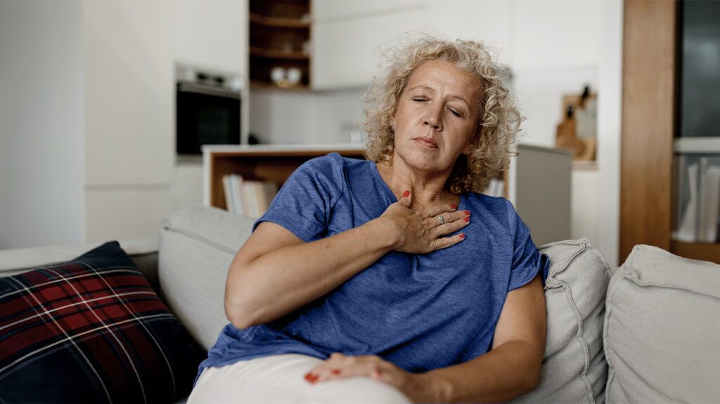 A woman with high cholesterol holding her chest and feeling symptoms of complications, such as angina.-1