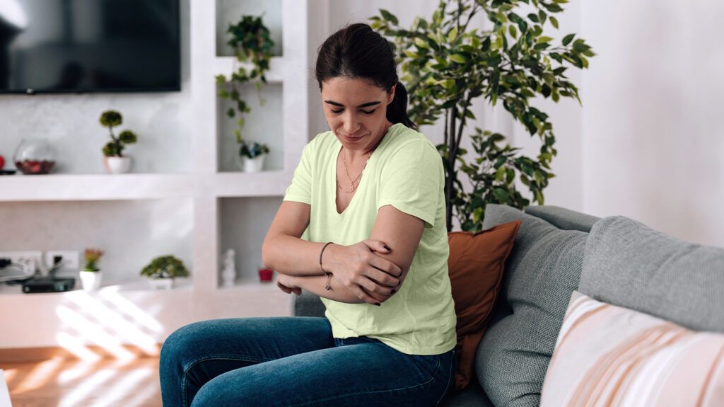Female sitting on a sofa holding her arm