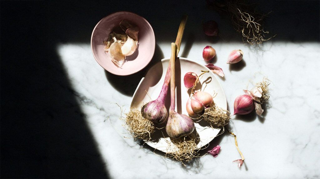 garlic bulbs on white plate, bowl, and table surface