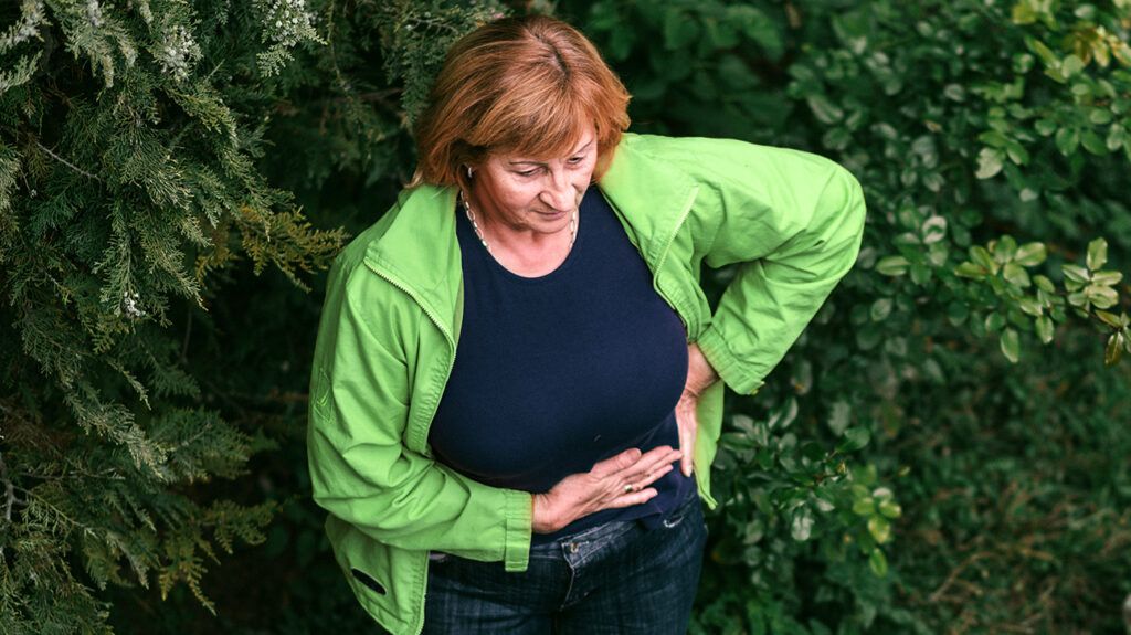 Woman with colitis holding her hands on her stomach.