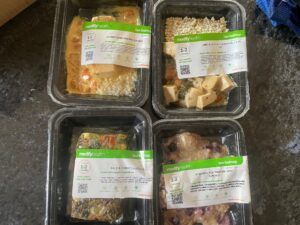 Four plastic cartons of pre-prepared meal kits from Modify Health lined up on kitchen counter