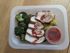 Chicken parmesan with broccoli florets in plastic tupperware tray with sauce sitting on kitchen countertop