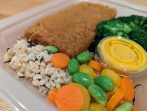 breaded tofu, green peas and carrots, and rice in plastic tupperware tray with sauce sitting on kitchen countertop