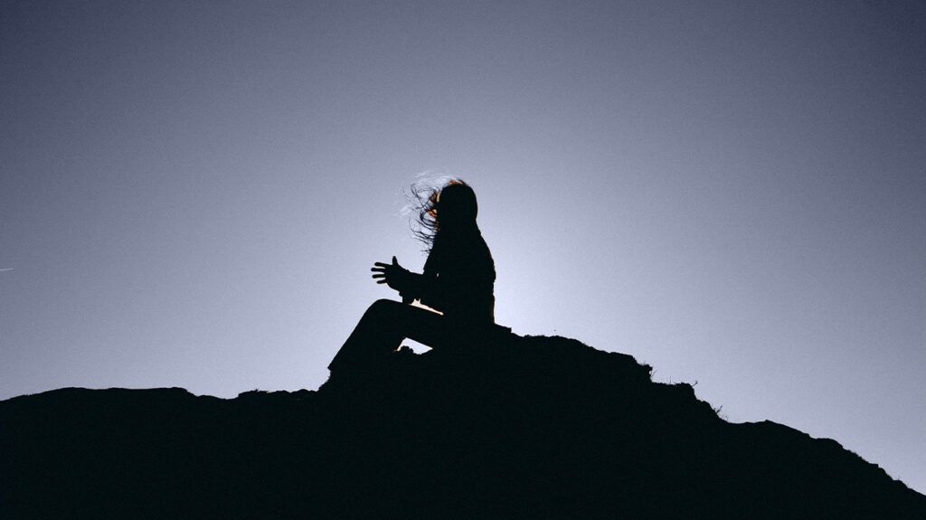 The silhouette of a woman sitting atop some rocks