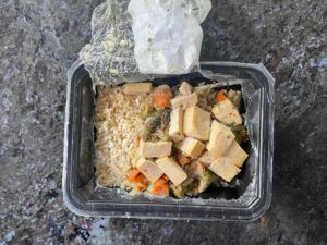 Open plastic carton of ModifyHealth meal kit with rice, vegetables, and chicken pieces, on kitchen countertop.