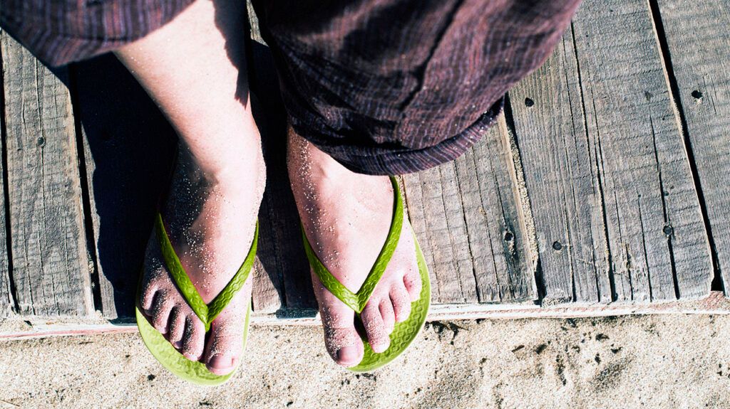 A pair of feet in flip flops with sand on them.