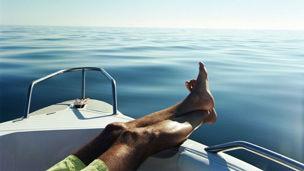 Person's legs and feet stretched over the side of a boat on a sunny day
