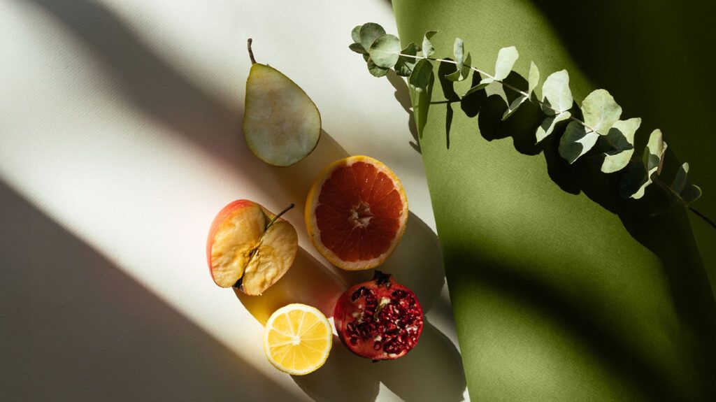 half a pear, apple, grapefruit, lemon, and pomegranate pictured against a green background