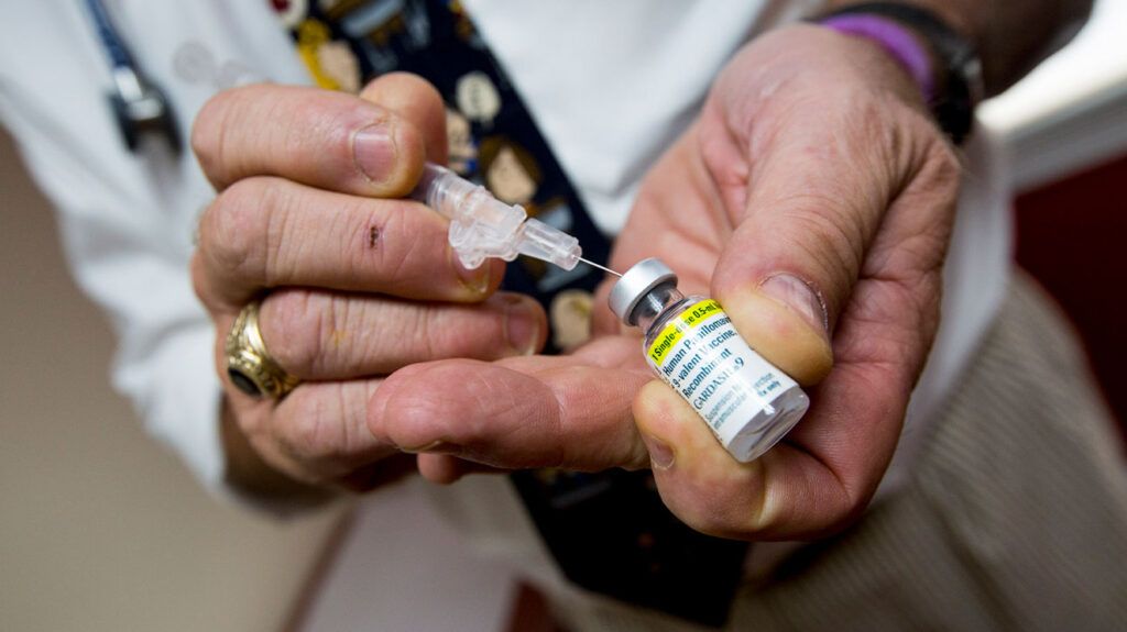 Close up of doctor's hands holding HPV vaccine vial and syringe