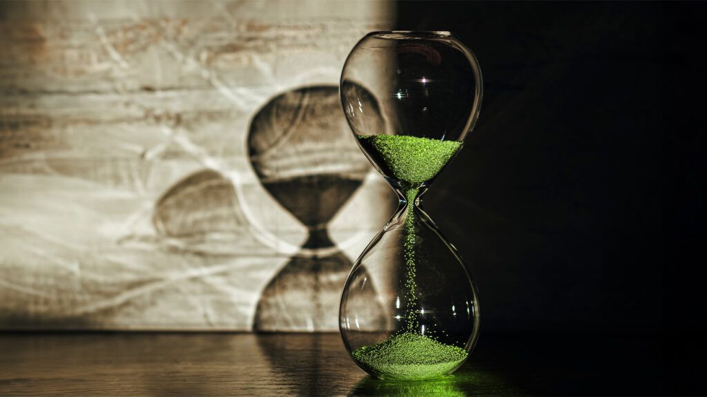 Hourglass with green sand and a shadow