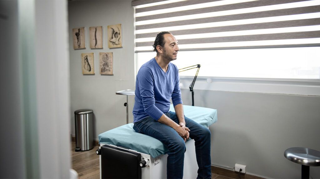 A man sat on a table in a doctor's office for a prostate cancer exam.