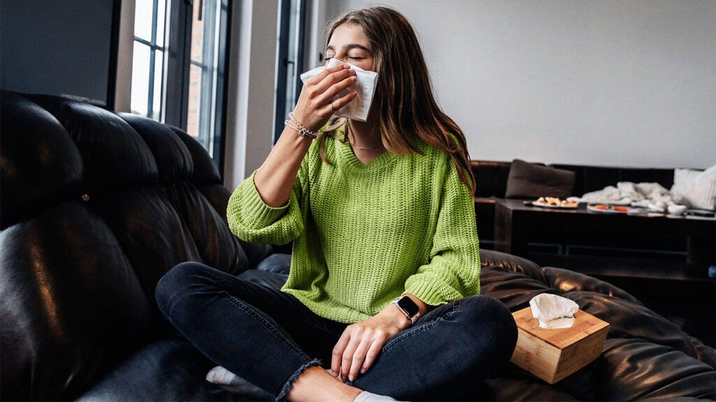 Female sitting on a sofa blowing her nose