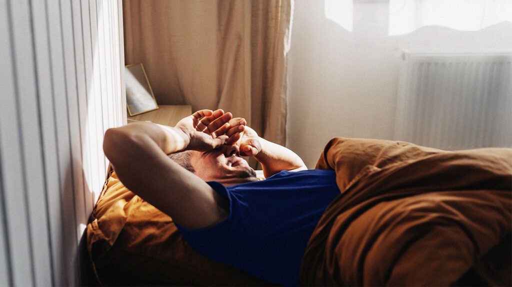 Male lying in bed with his arm over his face