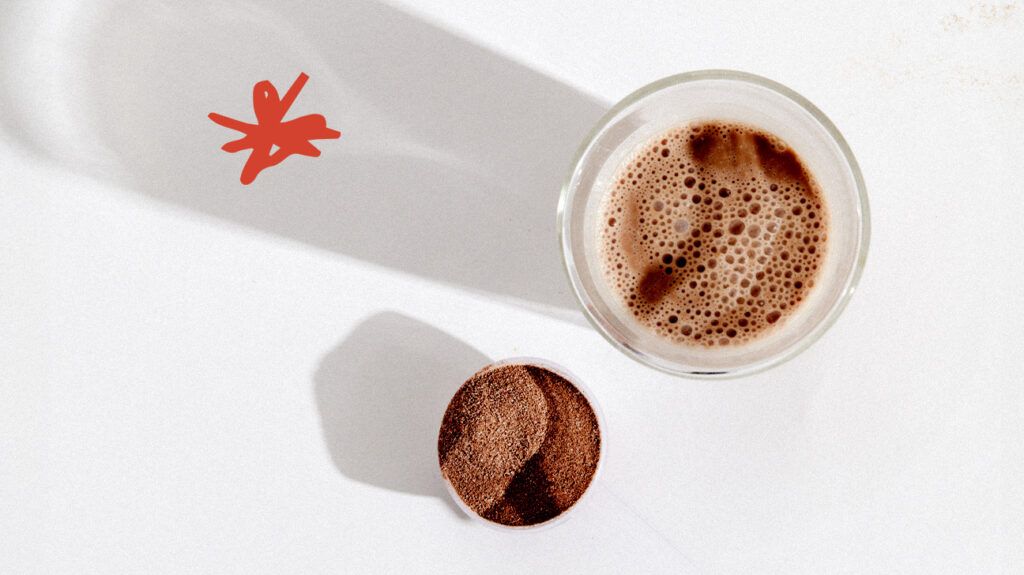 A protein shake in a glass next to some protein powder.-1