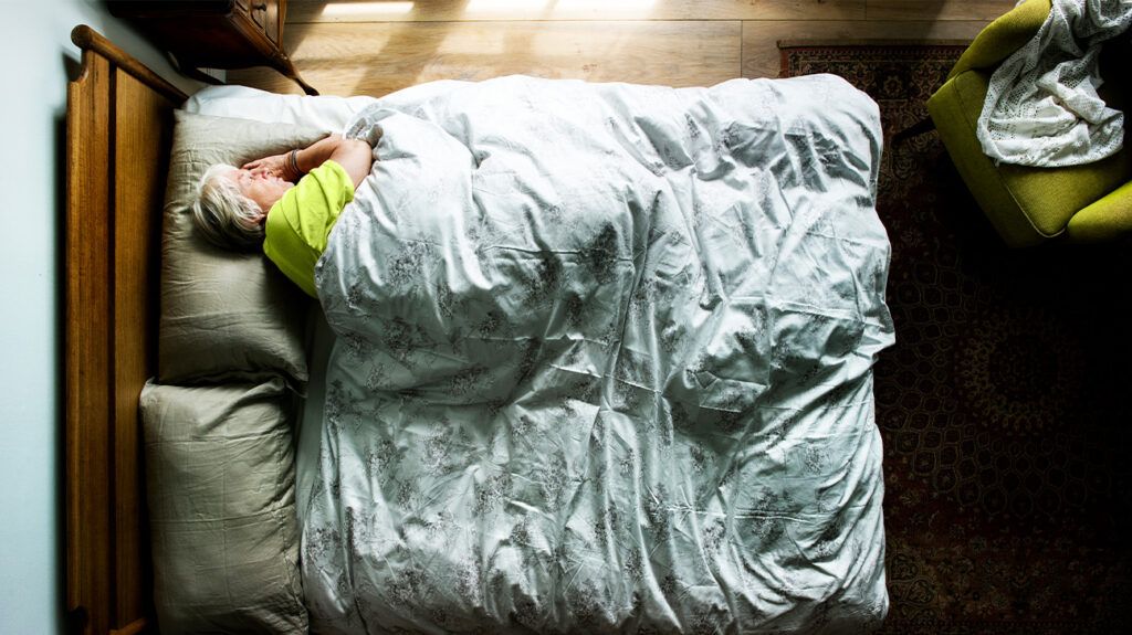 A bird's eye view of an older adult with dementia sleeping on their side in a bed.-1