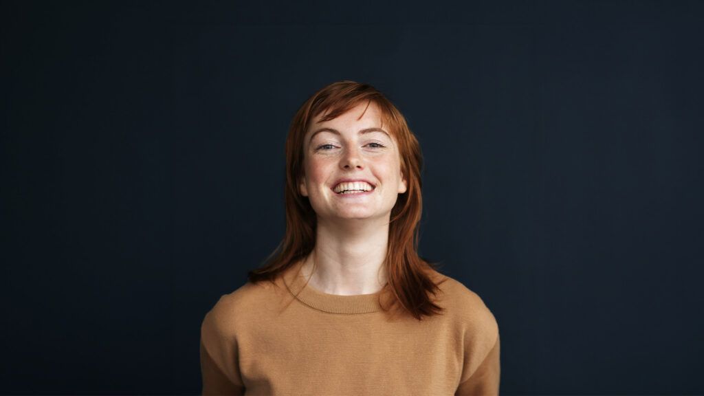 A portrait of a redheaded young woman smiling, to represent personality types. -1