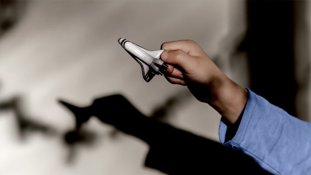 A child's hand holding a toy spaceship with a shadow beneath.-1