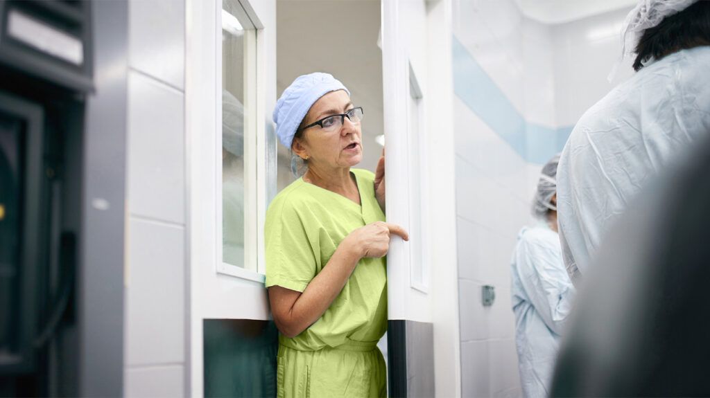 A female surgeon stands in the doorway of an operating room