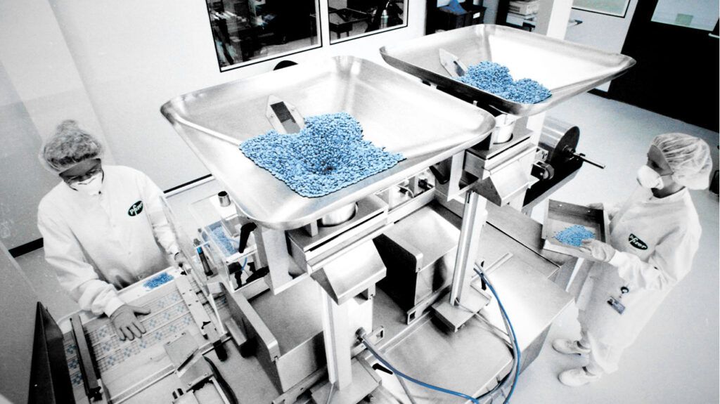 Two factory workers sorting out little blue pills of Viagra at a production factory
