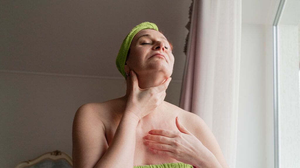 A woman in a towel touching her throat.