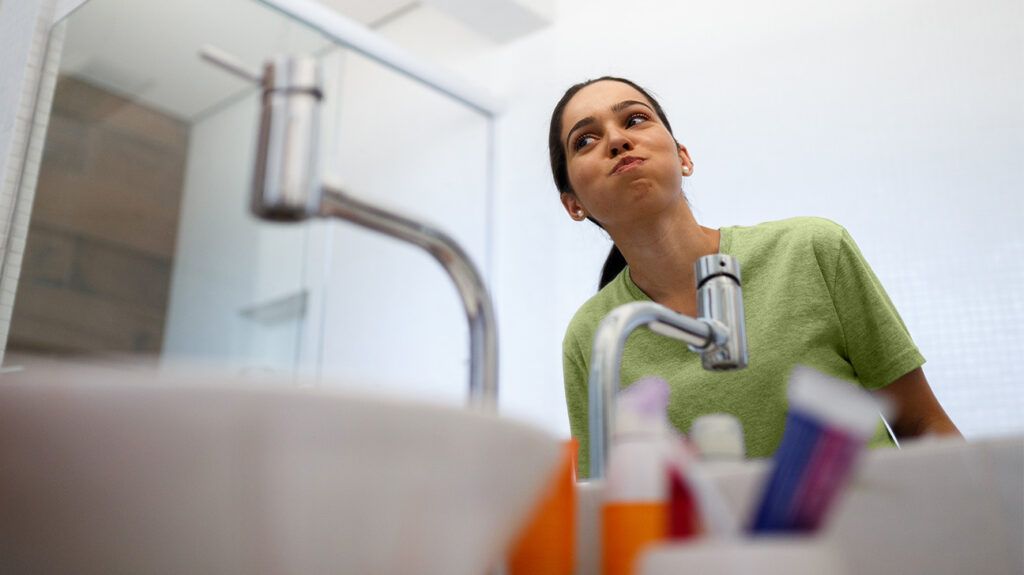 A younger woman in a bathroom uses mouthwash