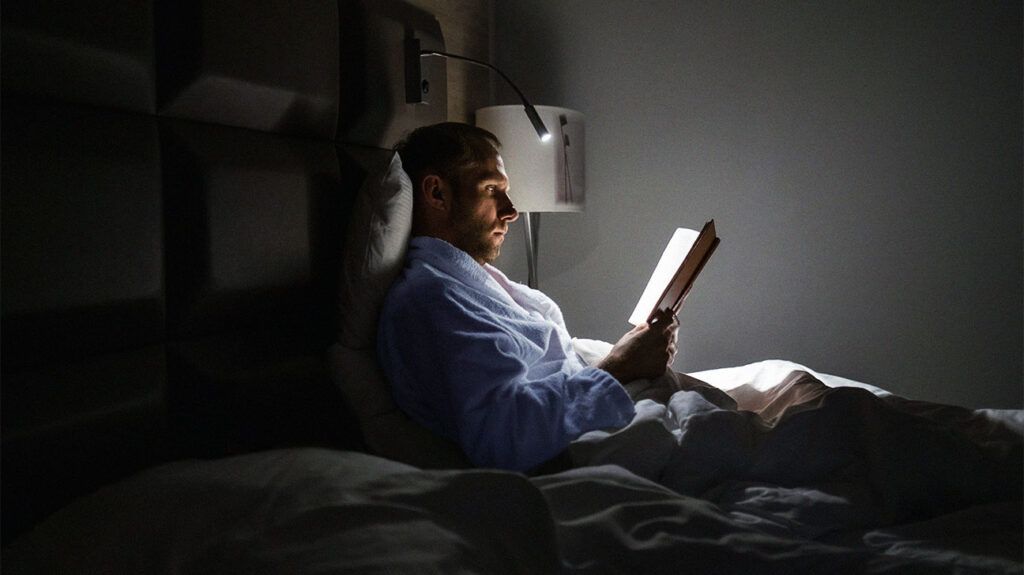 Male sitting up, reading in bed