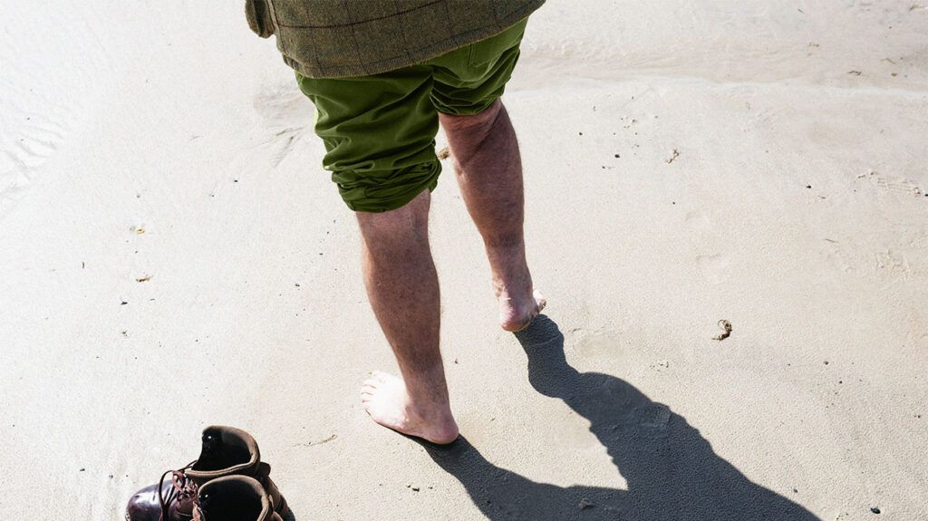 Closeup of a person standing barefoot on the beach.