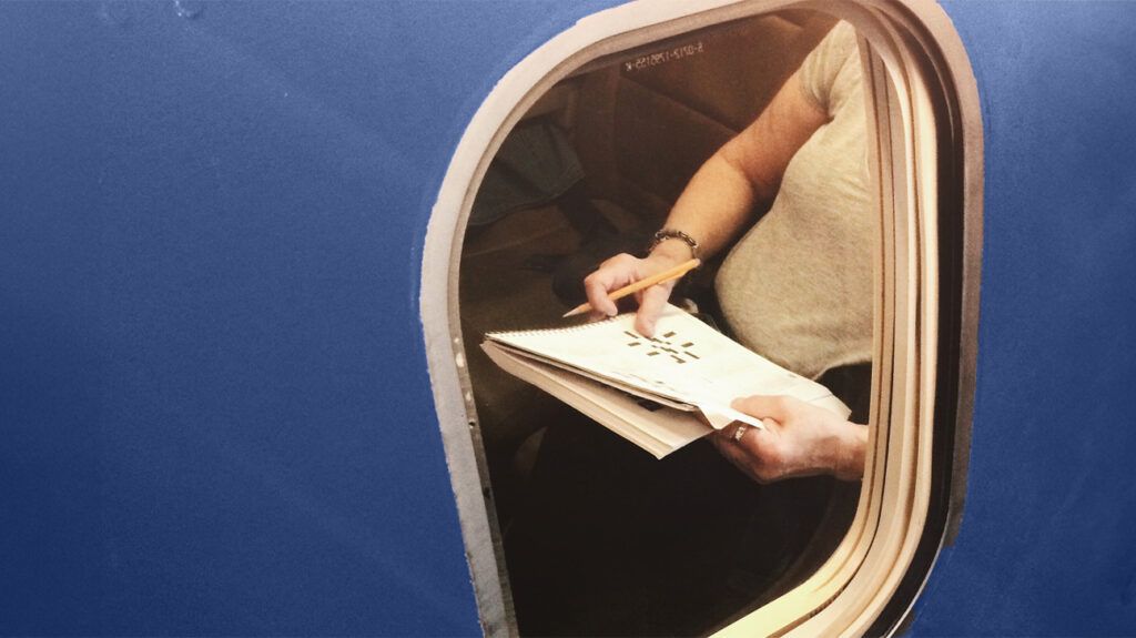 person solving crosswords in in newspaper viewed through plane window